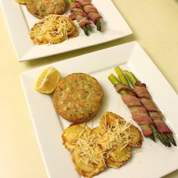 Image of a meal served on square white plates, lemon dill salmon patties, three cheese ravioli with a tomato/pesto sauce topped with parmesan, and bacon wrapped asparagus.