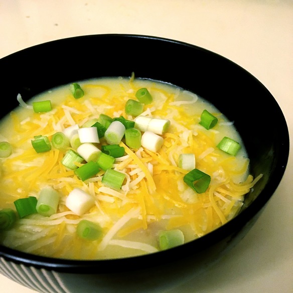 A black bowl containing creamy potato soup topped with grated cheddar cheese and chopped green onion.
